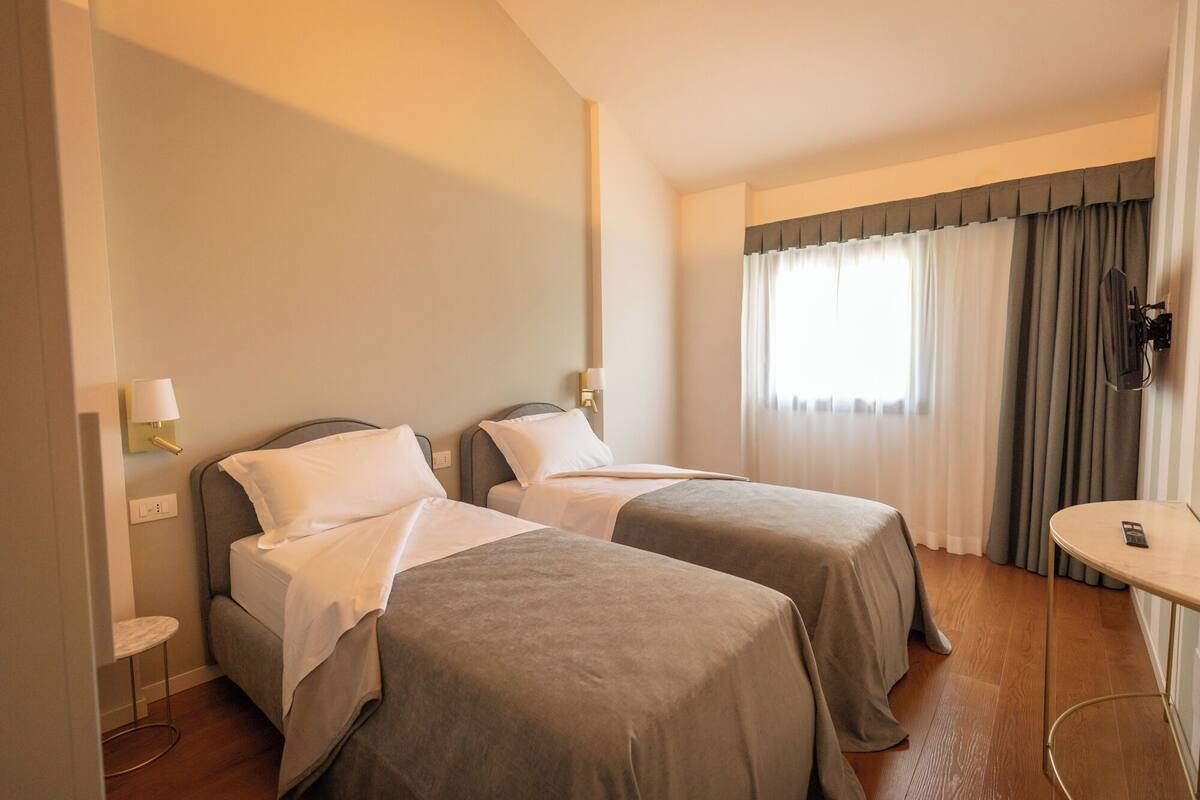 A hotel room with two beds, a small table, and a window with curtains.