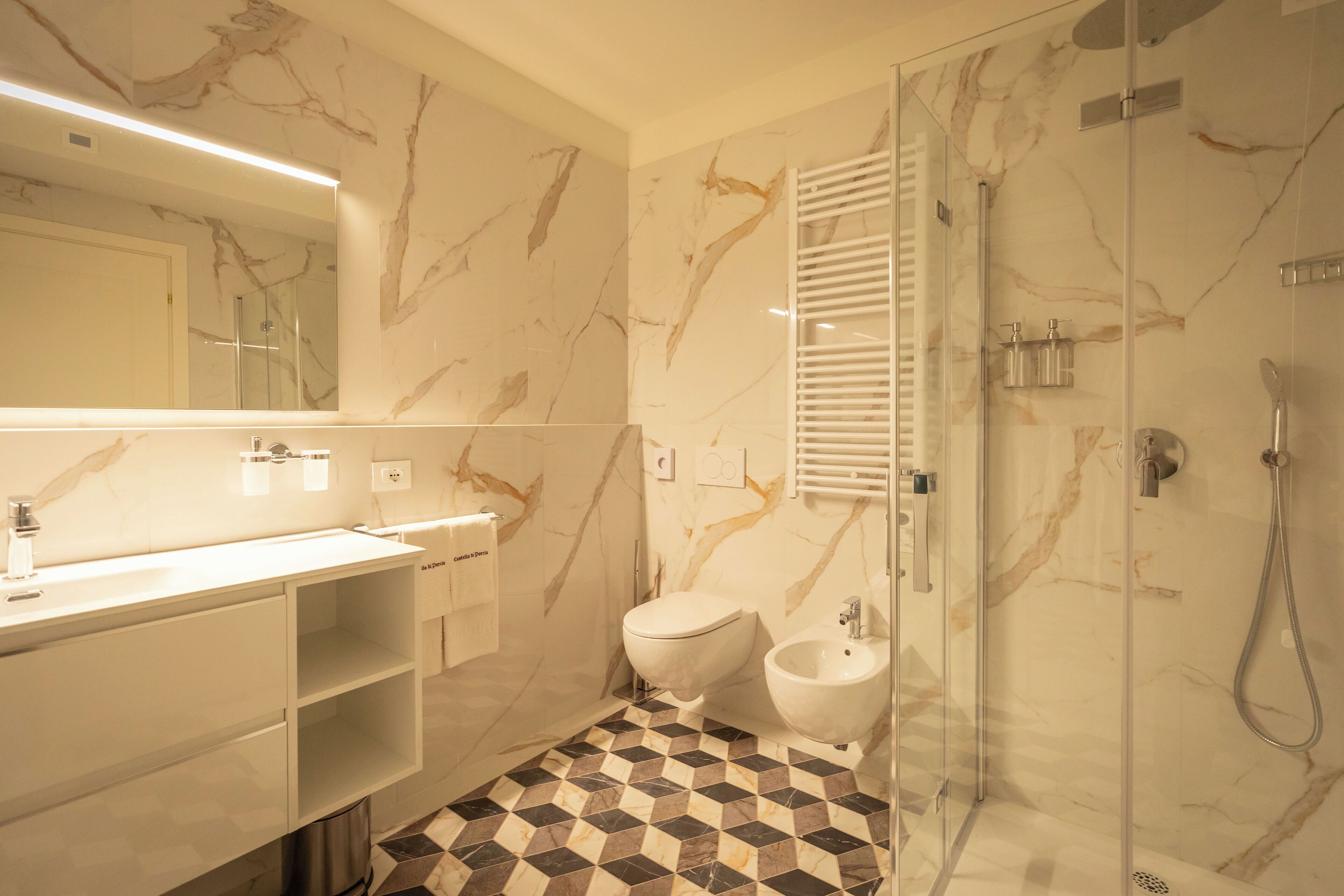 Un baño moderno con salpicadero de mármol, ducha con mampara de vidrio, un bidé y un lavabo con espejo.