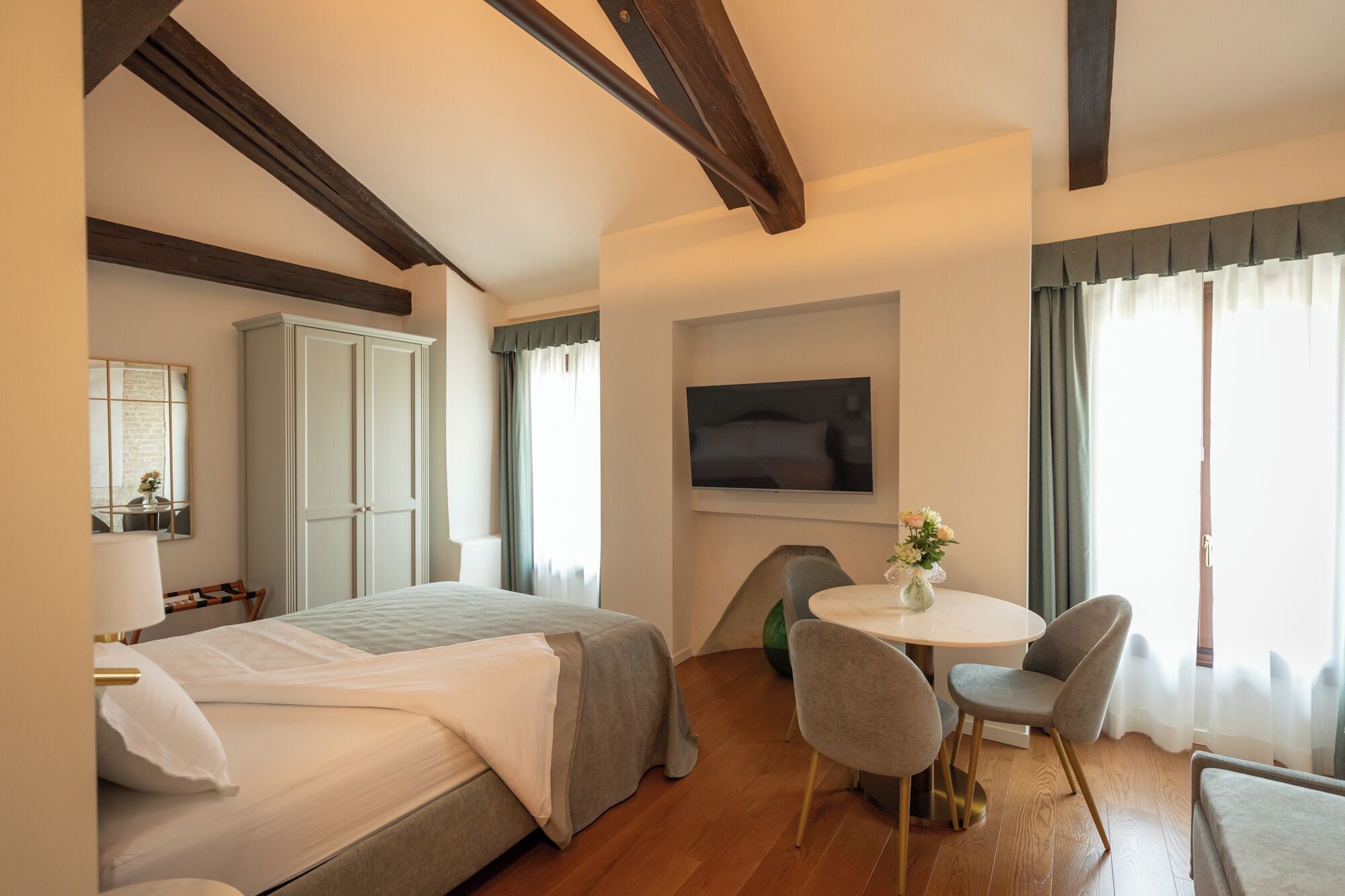 A hotel room with a bed, a desk with chairs, a television, and a window with curtains.