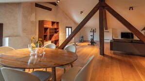 Un loft amplio con una mesa de comedor de madera, sillas, una estantería, una bicicleta estática y un televisor.