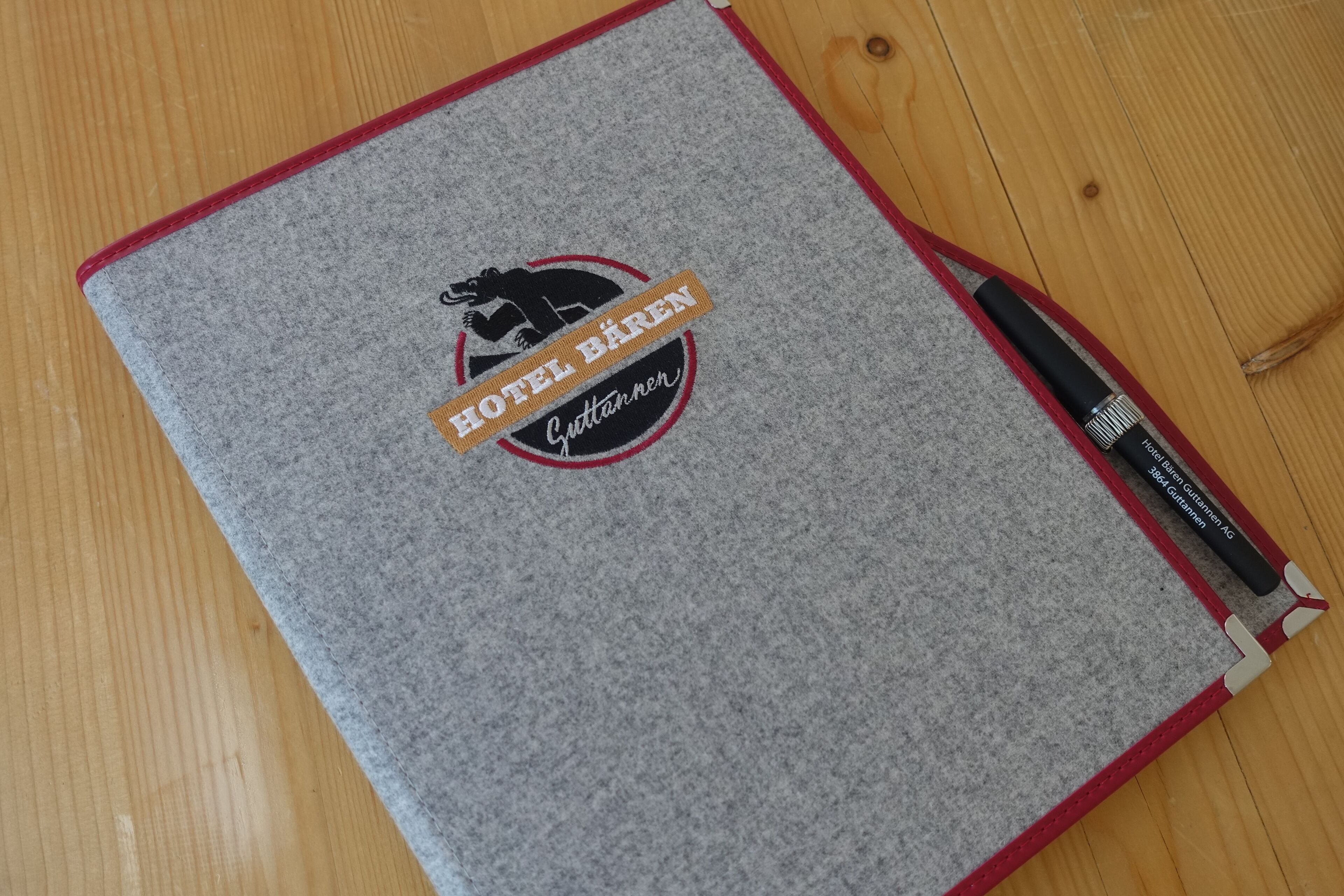 Een notitieboekje met een logo en tekst op de omslag, op een houten ondergrond.