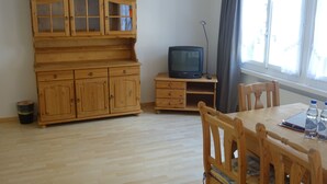 A room with a wooden cabinet, a television on a small table, a chair, and a window with curtains. - Hotel Bären Guttannen (Guttannen)