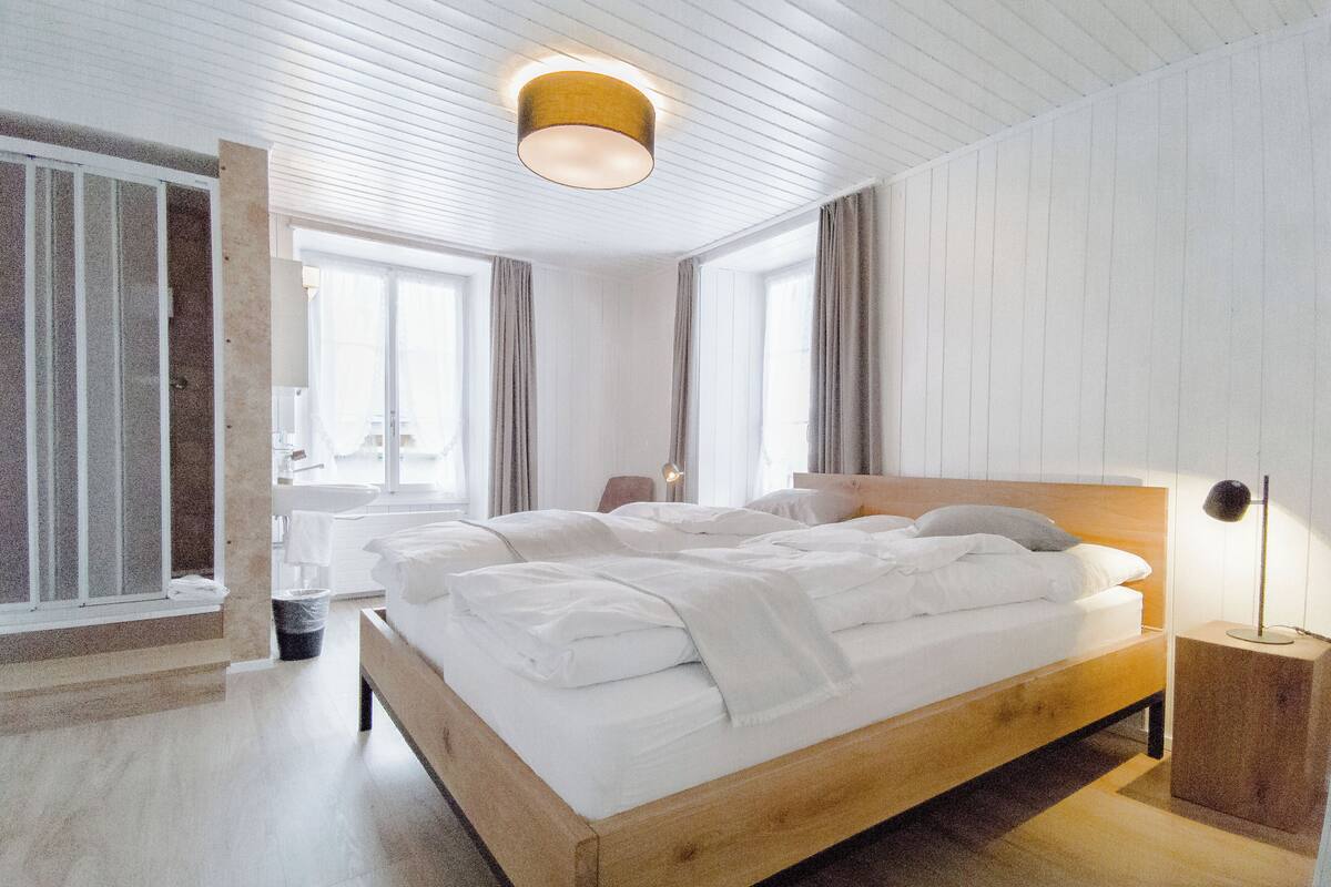 Un dormitorio moderno con una cama de madera, una mesita de noche, una lámpara de pie y una ventana con cortinas.