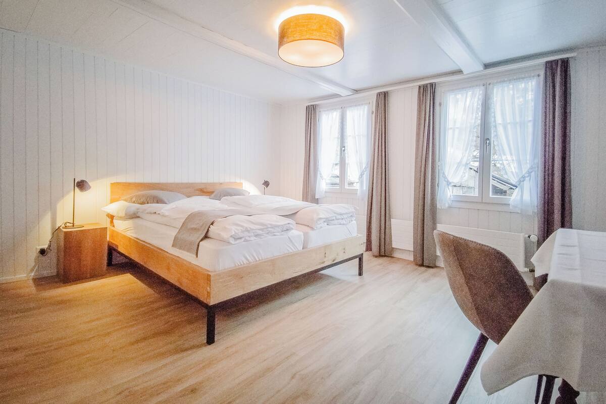 Un dormitorio con cama, mesita de noche, lámpara y ventana con cortinas.
