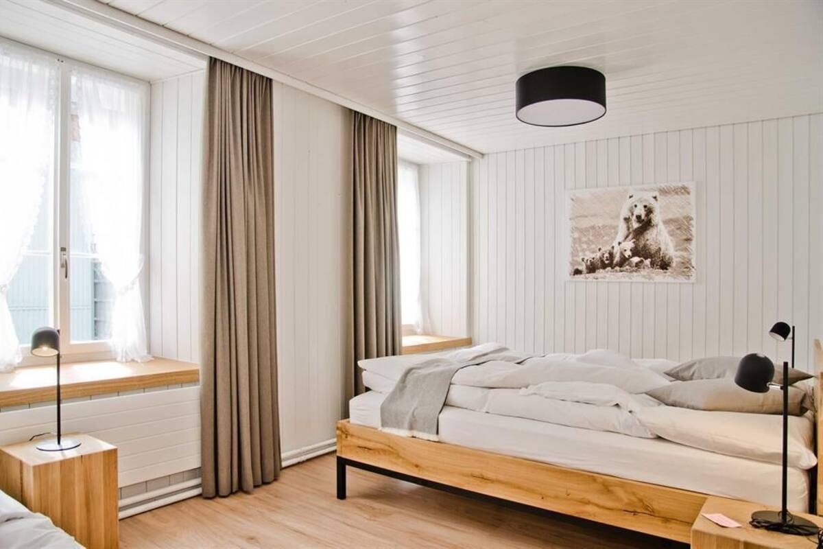 Un dormitorio con una cama de madera, una ventana con cortinas, una mesita de noche y una lámpara de pared.