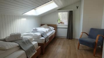 Une chambre avec deux lits, une fenêtre avec des rideaux, une chaise et une lucarne.