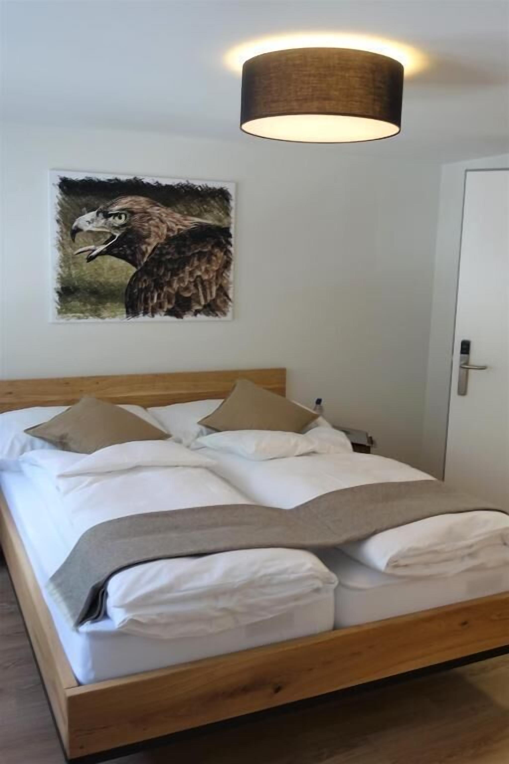 Een netjes opgemaakt bed met witte en grijze linnens, een houten hoofdbord en een schilderij van een adelaar aan de muur.