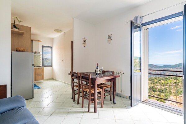 A dining area with a table and chairs, a refrigerator, a kitchen area, and a large window with a view.