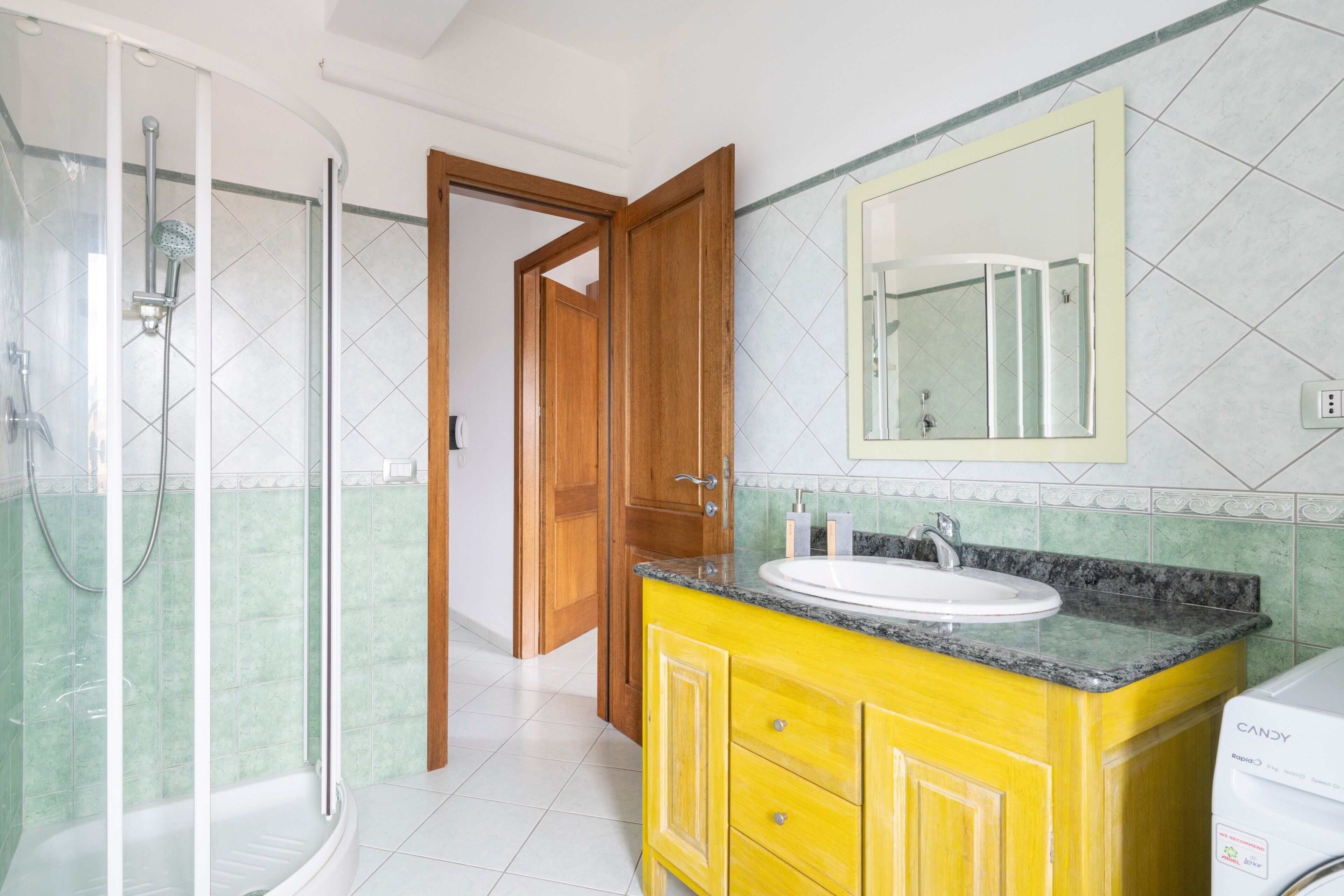 Un bagno con doccia, lavandino, specchio e porta in legno.