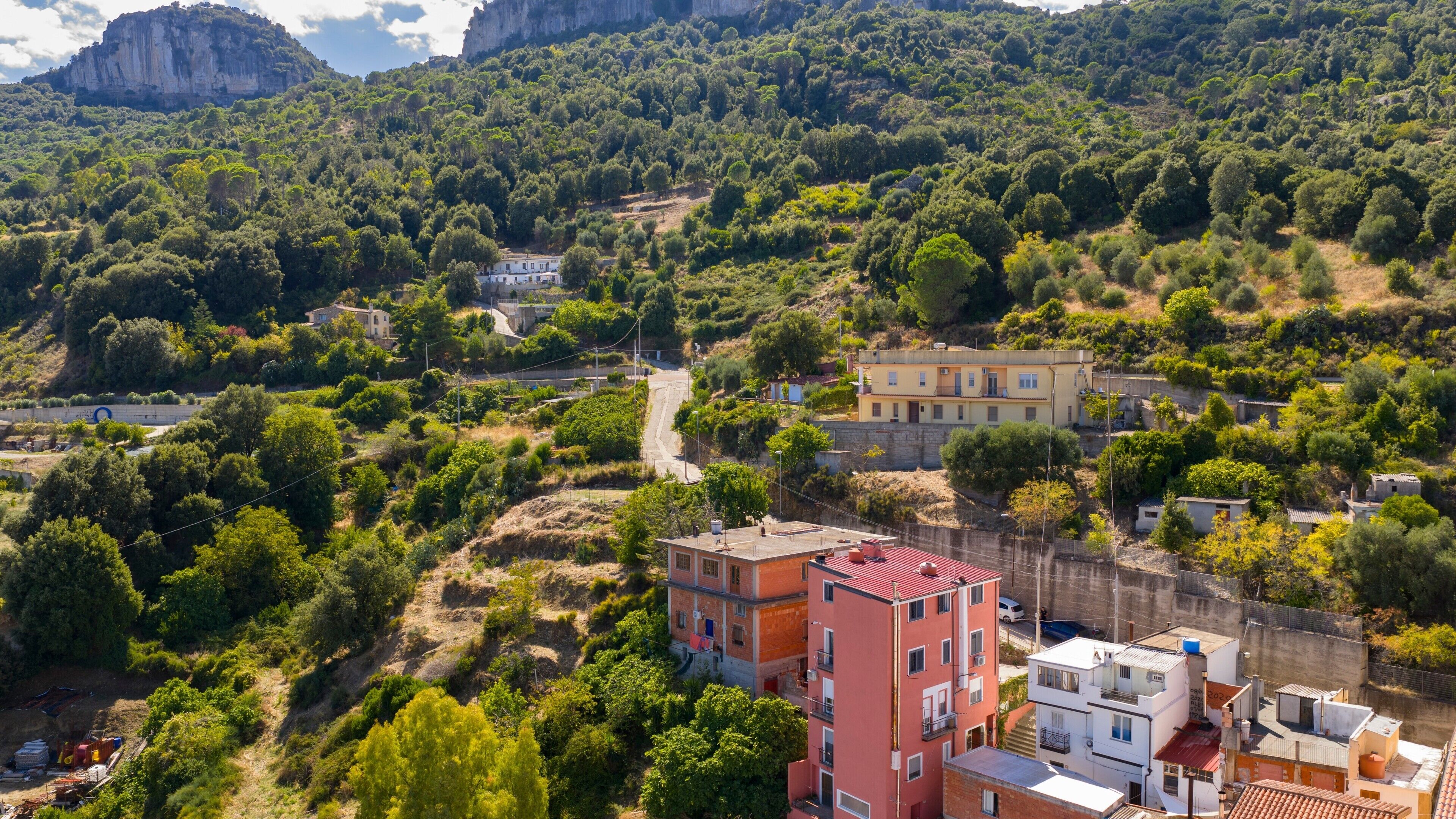 A hillside residential area with buildings, a road, and dense vegetation.