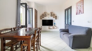 A dining area with a wooden table and chairs, a grey sofa, and a TV mounted on the wall.