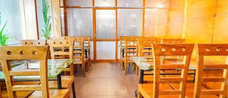 Un restaurant avec des chaises et des tables en bois, un mur recouvert de carreaux et une grande fenêtre.