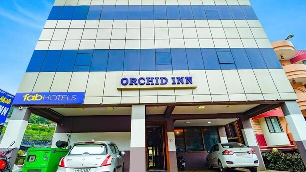 Un hôtel appelé Orchid Inn, doté d’une façade moderne, d’une entrée bien visible et d’un parking où sont garées des voitures.
