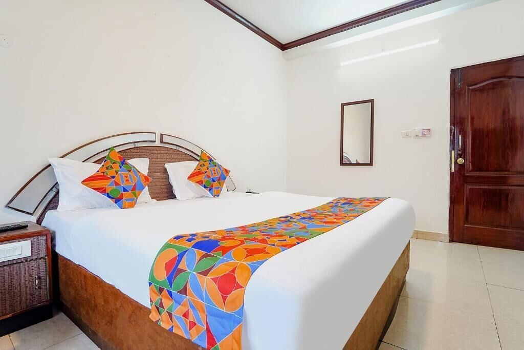 Una cama bien tendida con un edredón de estampado geométrico y colores vivos, un cabecero de madera y una mesita de noche con una lámpara.
