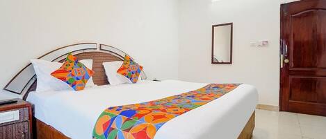 Una cama bien tendida con un edredón de estampado geométrico y colores vivos, un cabecero de madera y una mesita de noche con una lámpara.