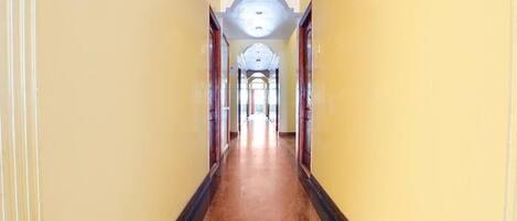 A long, narrow hallway with yellow walls and a wooden floor, leading to a grand archway at the end.