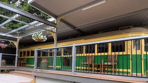A covered outdoor seating area with a green and yellow bus as a backdrop. - Yarra Valley Tram Stay (Lilydale)