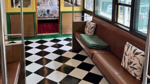 A train interior with a checkered floor, wooden paneling, a bench with cushions, and hanging handrails. - Yarra Valley Tram Stay (Lilydale)