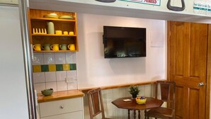 A compact kitchen with a wooden countertop, a dining table with chairs, a television mounted on the wall, and a checkered floor. - Yarra Valley Tram Stay (Lilydale)