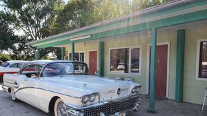 A vintage white car parked in front of a building with numbered doors and windows.