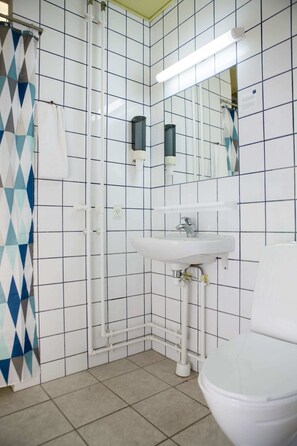 A bathroom with a white sink, a toilet, and a shower area with a patterned curtain. - Wittrups Motel (Albertslund)
