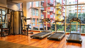 A gym with treadmills, weight machines, and a large window with a view of colorful buildings.