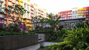 A modern apartment complex with colorful buildings, a landscaped garden with various plants, and a paved walkway.