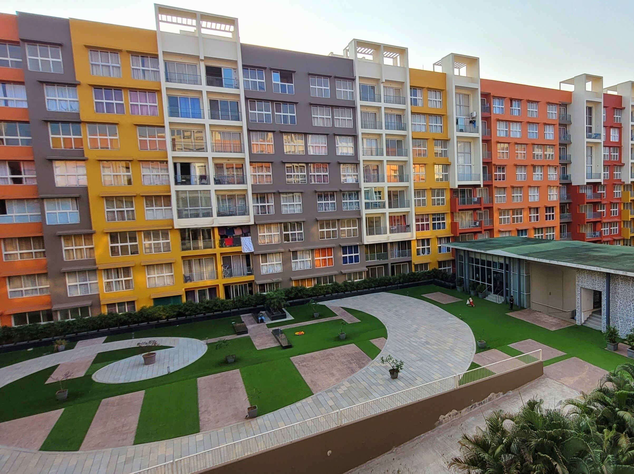 A multi-story residential building with balconies and a central courtyard with green lawns and pathways.