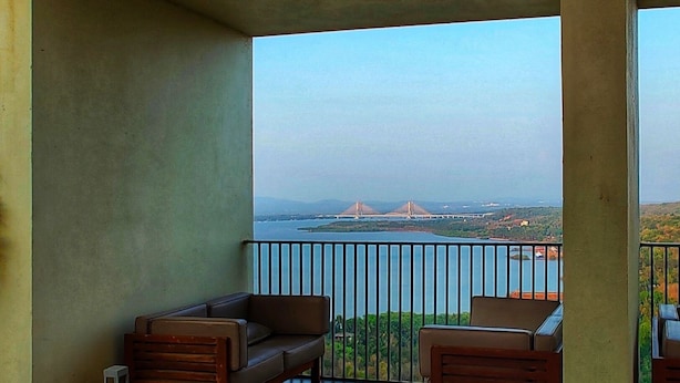 A balcony with a sofa and chairs, overlooking a body of water and a bridge.