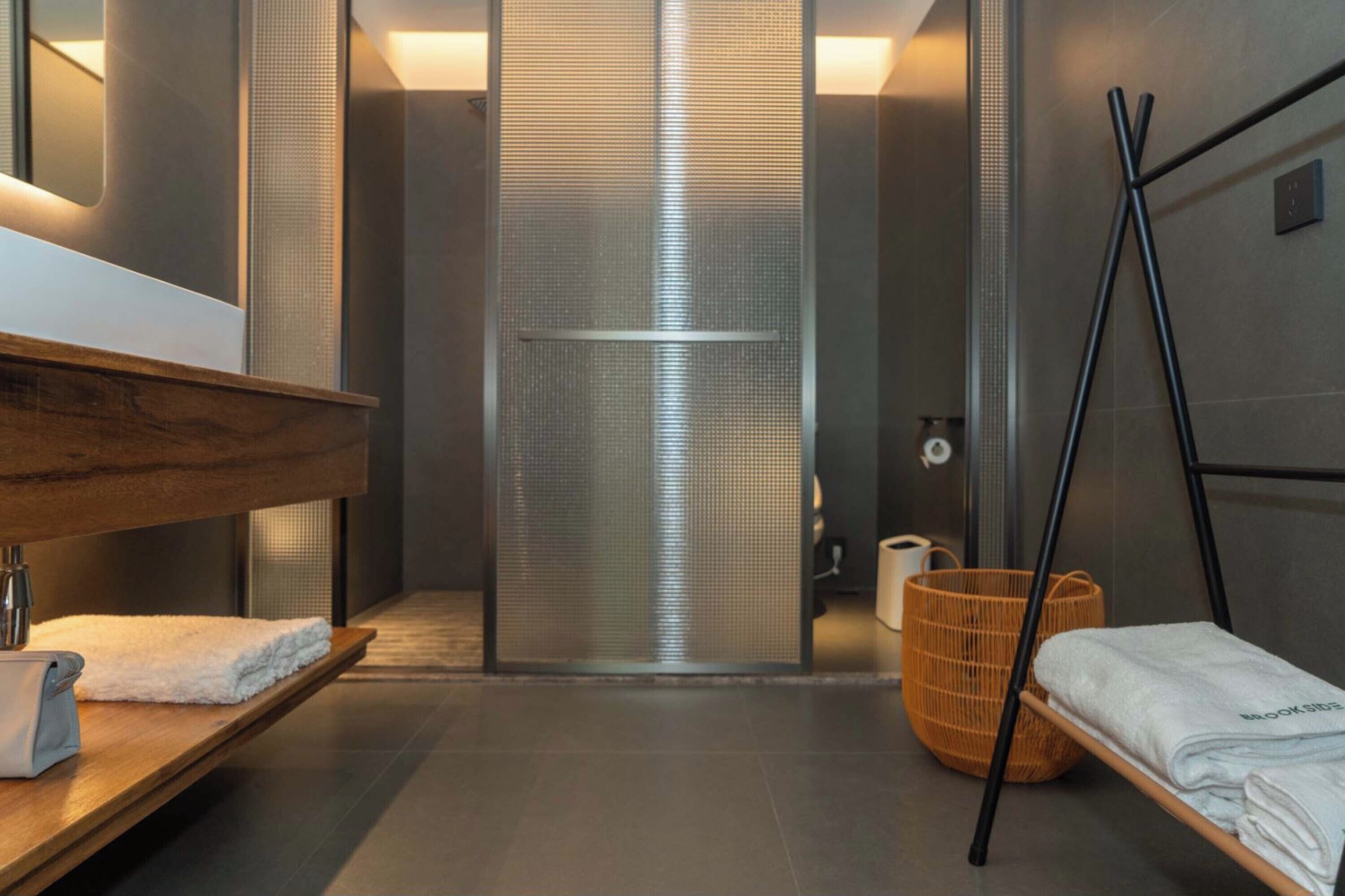 A modern bathroom with a wooden bench, a large mirror, a shower enclosure, and a towel rack.