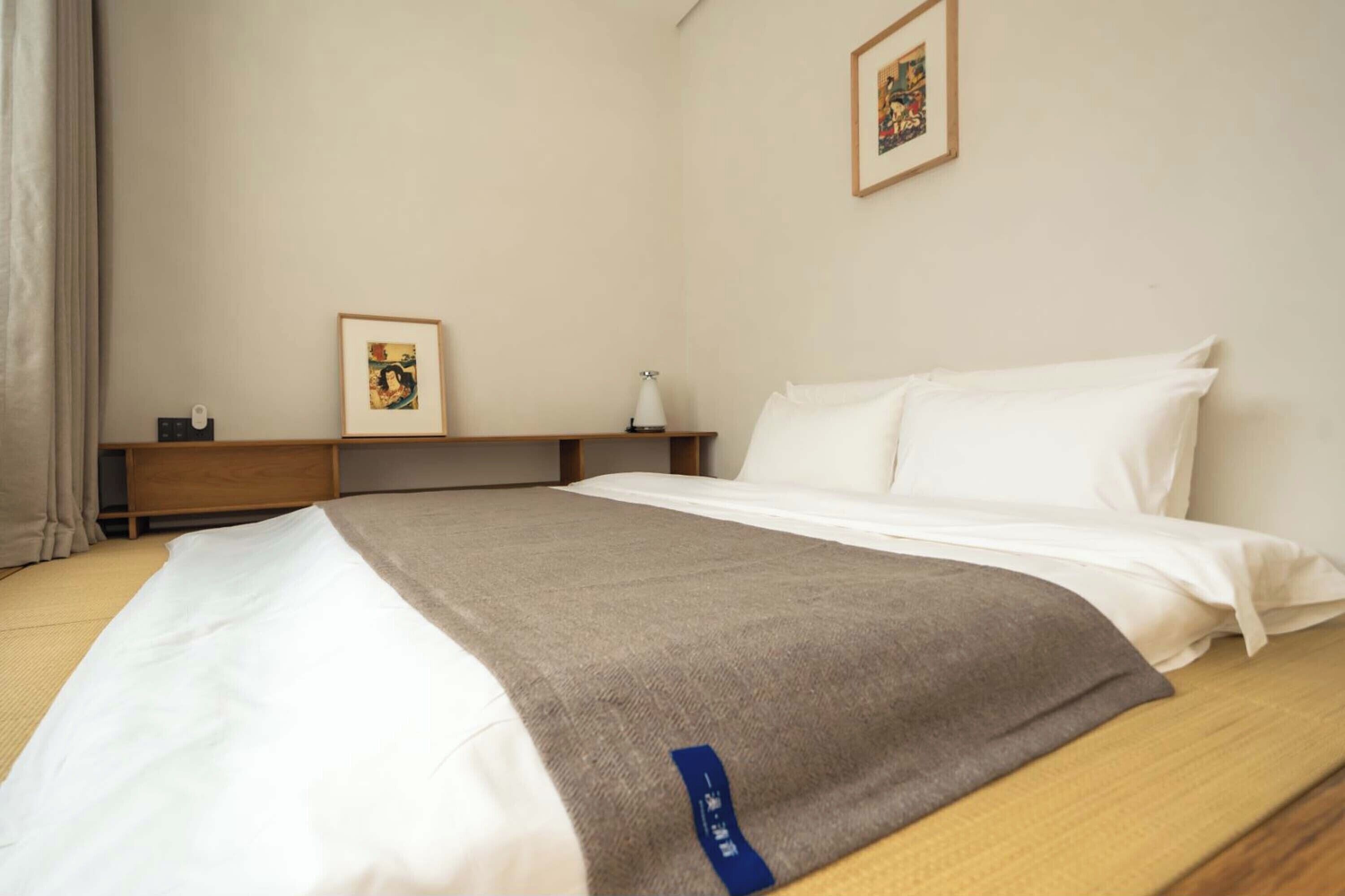 A hotel room with a neatly made bed, a bedside table with a lamp, and a framed picture on the wall.