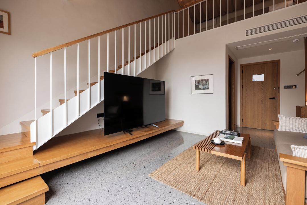 Una sala de estar moderna con una escalera de madera, un televisor de pantalla plana, una mesa de centro y un sofá.