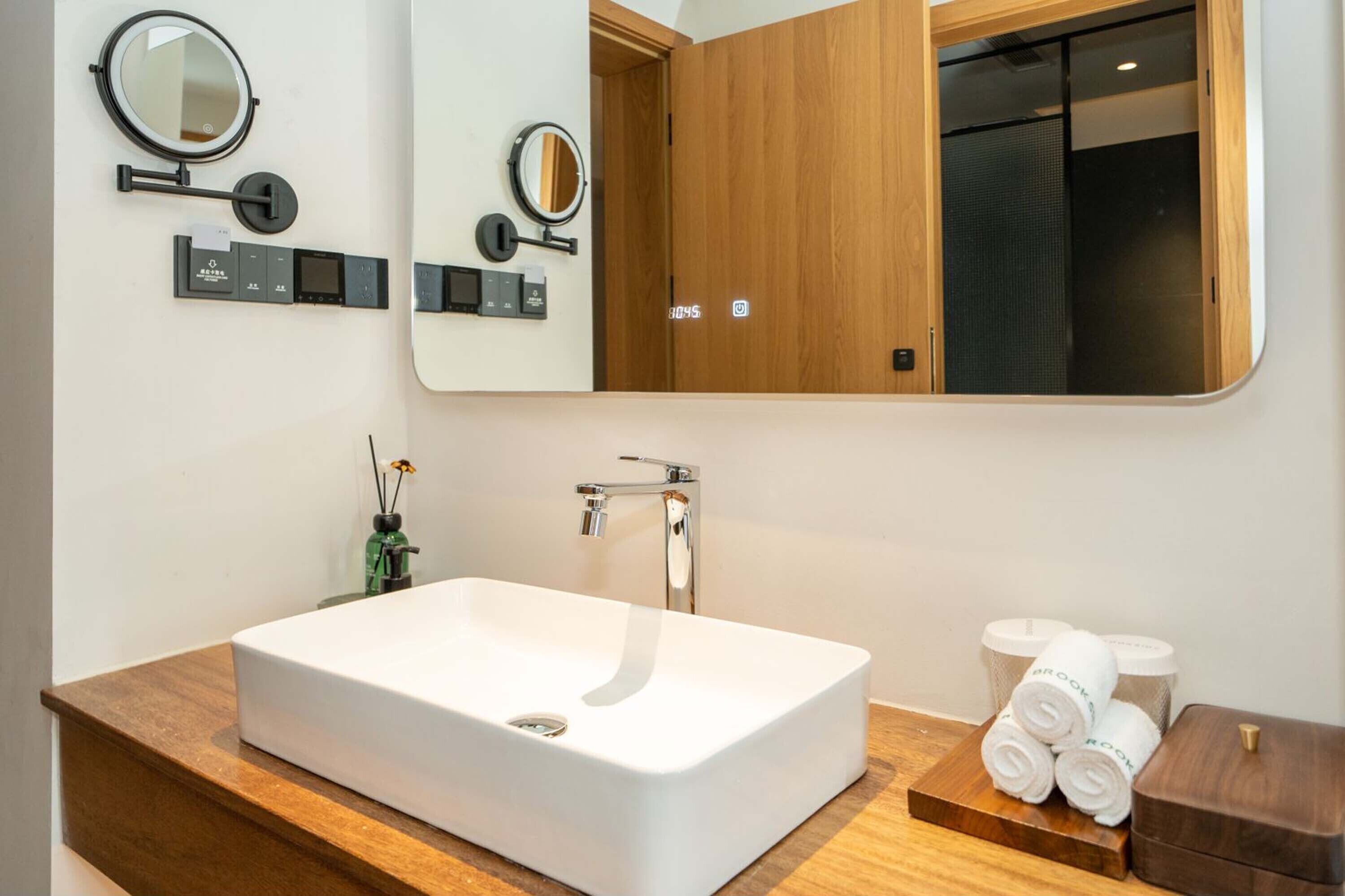 Un baño moderno con un lavamanos grande y rectangular, dos espejos adosados a la pared, un mueble de tocador de madera y un dispensador de toallas.