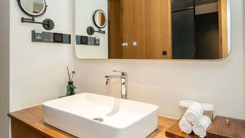 Un baño moderno con un lavamanos grande y rectangular, dos espejos adosados a la pared, un mueble de tocador de madera y un dispensador de toallas.