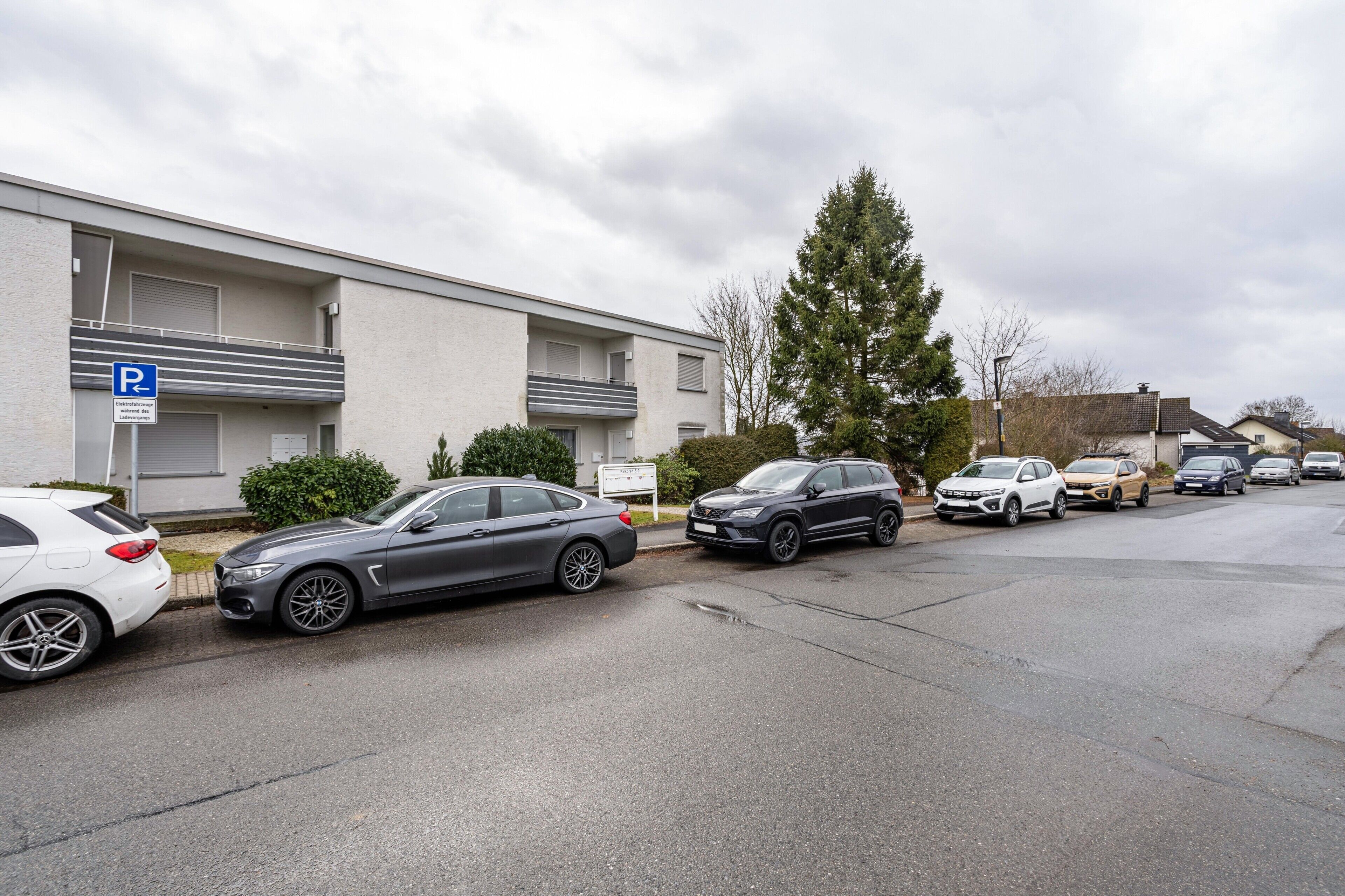 A parking lot with cars parked in front of a building with a balcony.