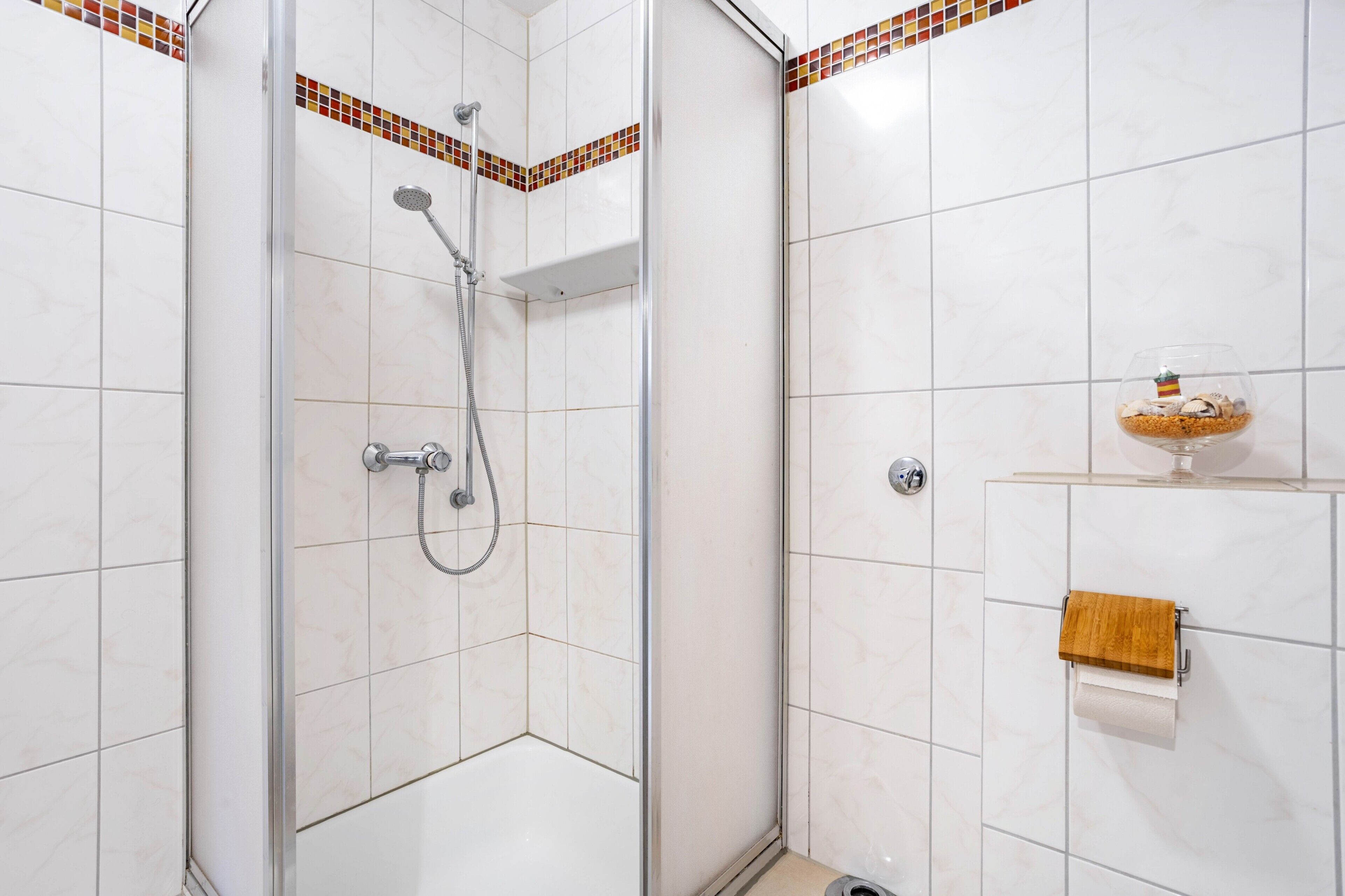 A shower area with a glass door, a towel rack with a wooden towel, and a small shelf with a decorative item.