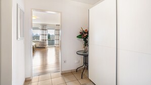 Een gang met uitzicht op een balkon, een tafeltje met een plant en een deur naar een andere kamer.