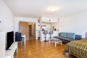 Un salon moderne comprenant un canapé, un téléviseur, un coin repas avec des chaises et un espace cuisine.