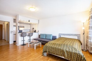 Habitación de hotel compacta con cama, sofá, pequeña cocina y mesa de comedor.