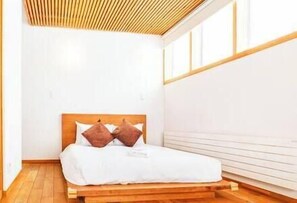 A bedroom with a wooden bed frame, white bedding, and a slatted wooden ceiling.