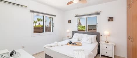 A bedroom with a bed, bedside tables, a ceiling fan, and windows with blinds.