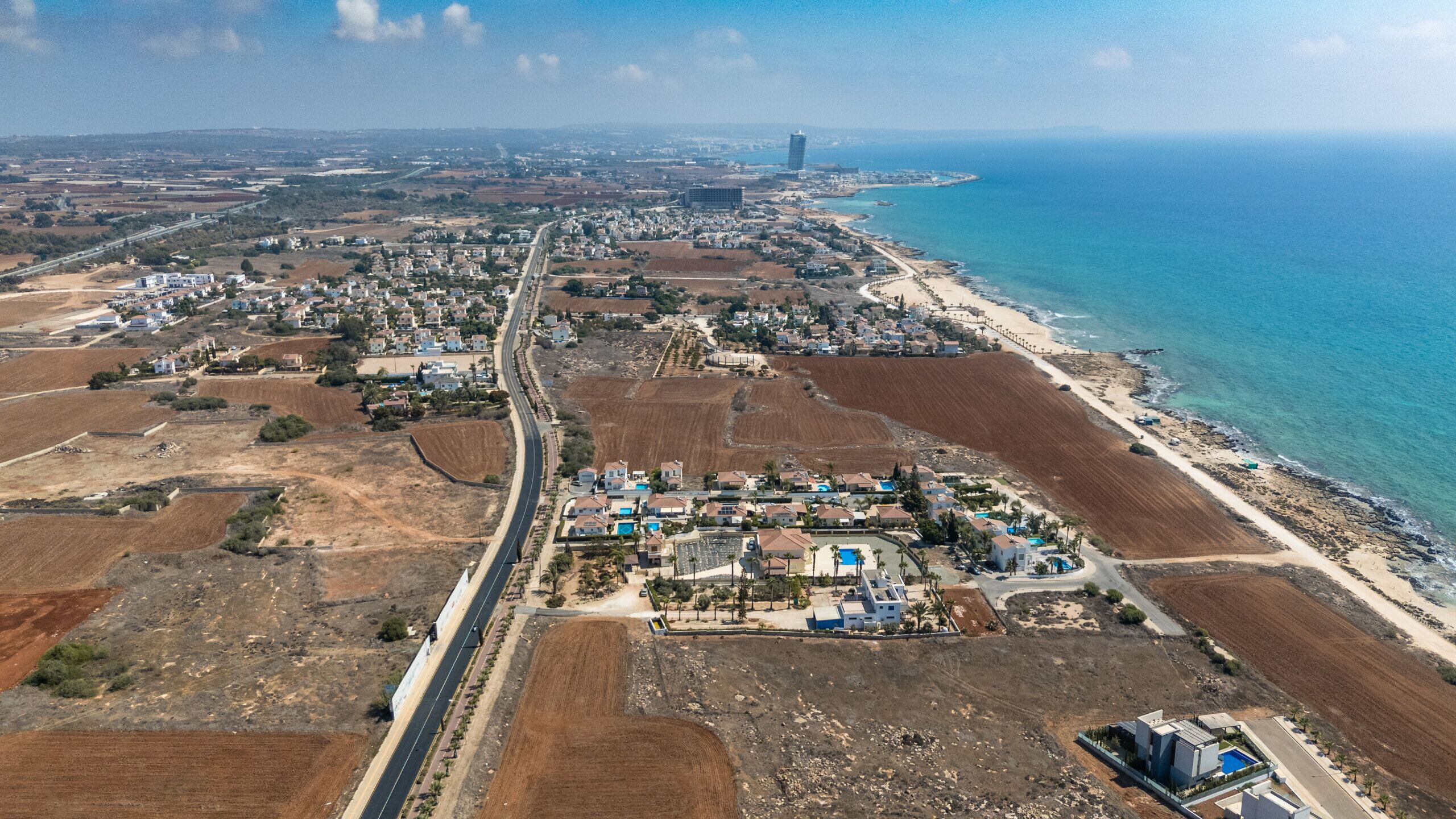 Vue aérienne d’une ville côtière, avec une route principale, des quartiers résidentiels et une plage.