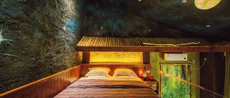Un lit recouvert d’une couvre-lit à rayures, une fresque représentant un ciel étoilé au plafond, et une lune figurant dans cette fresque.