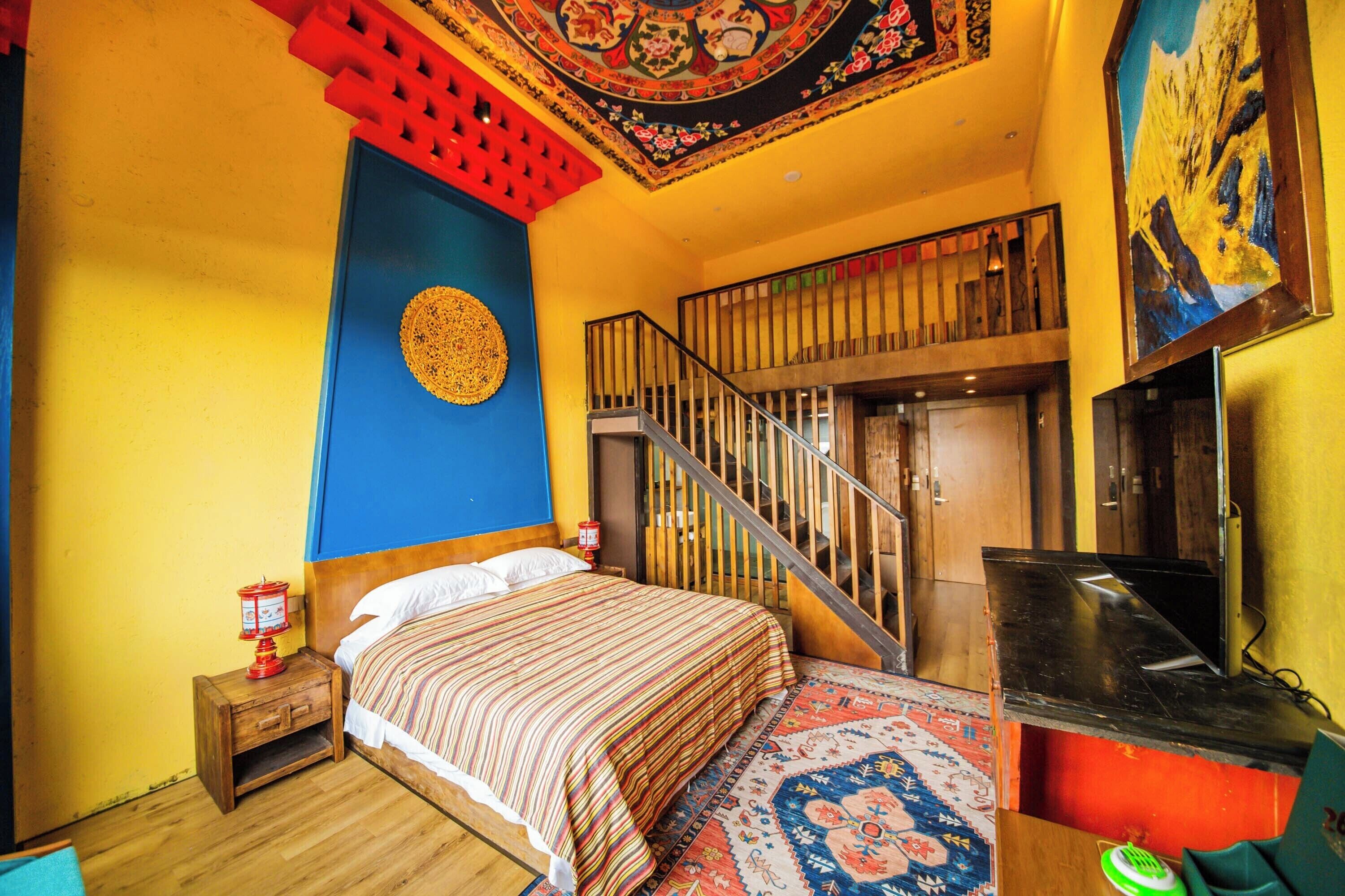 A room with a bed, a small table with a lamp, a staircase, and a TV.