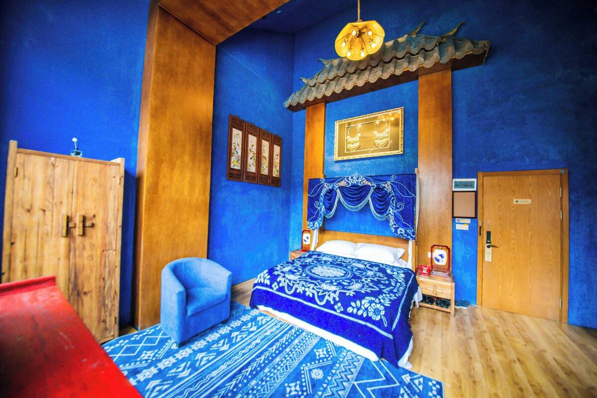 A room with a bed, a wooden wardrobe, a chair, and a traditional ceiling design.
