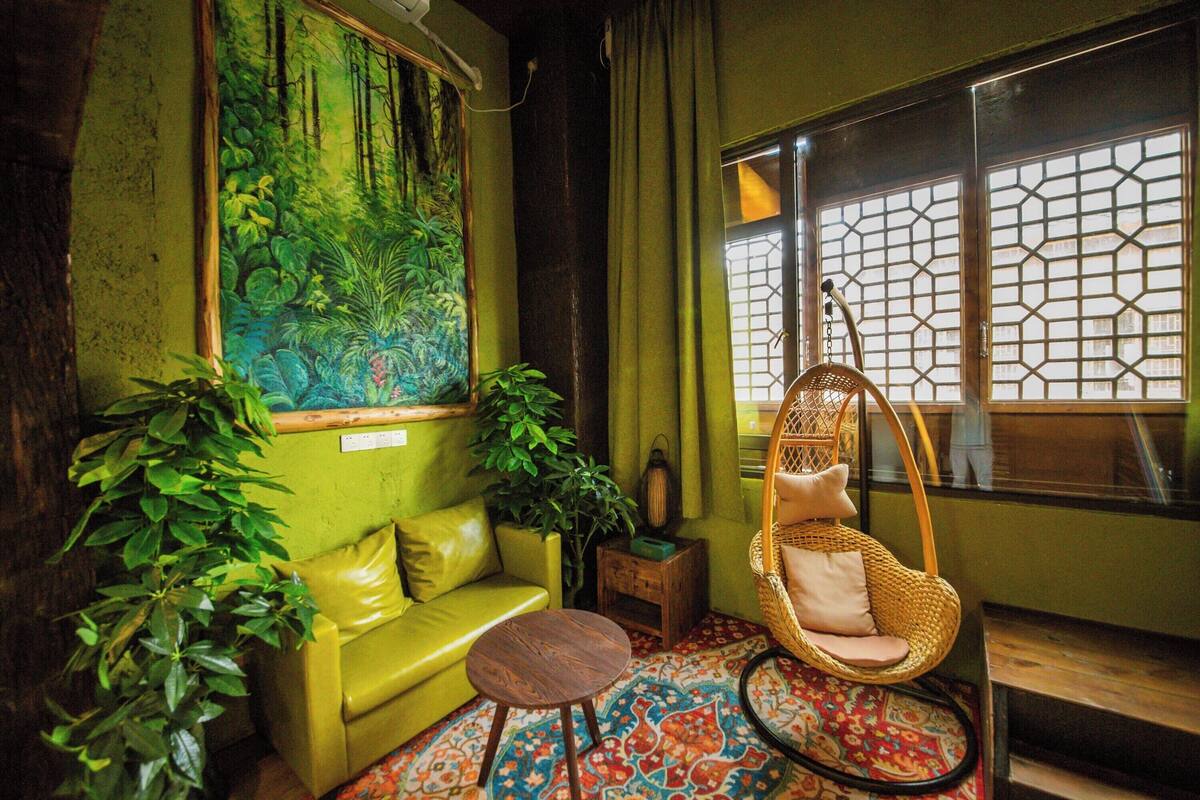 A room with a green sofa, a hanging chair, and a large window with a geometric pattern.