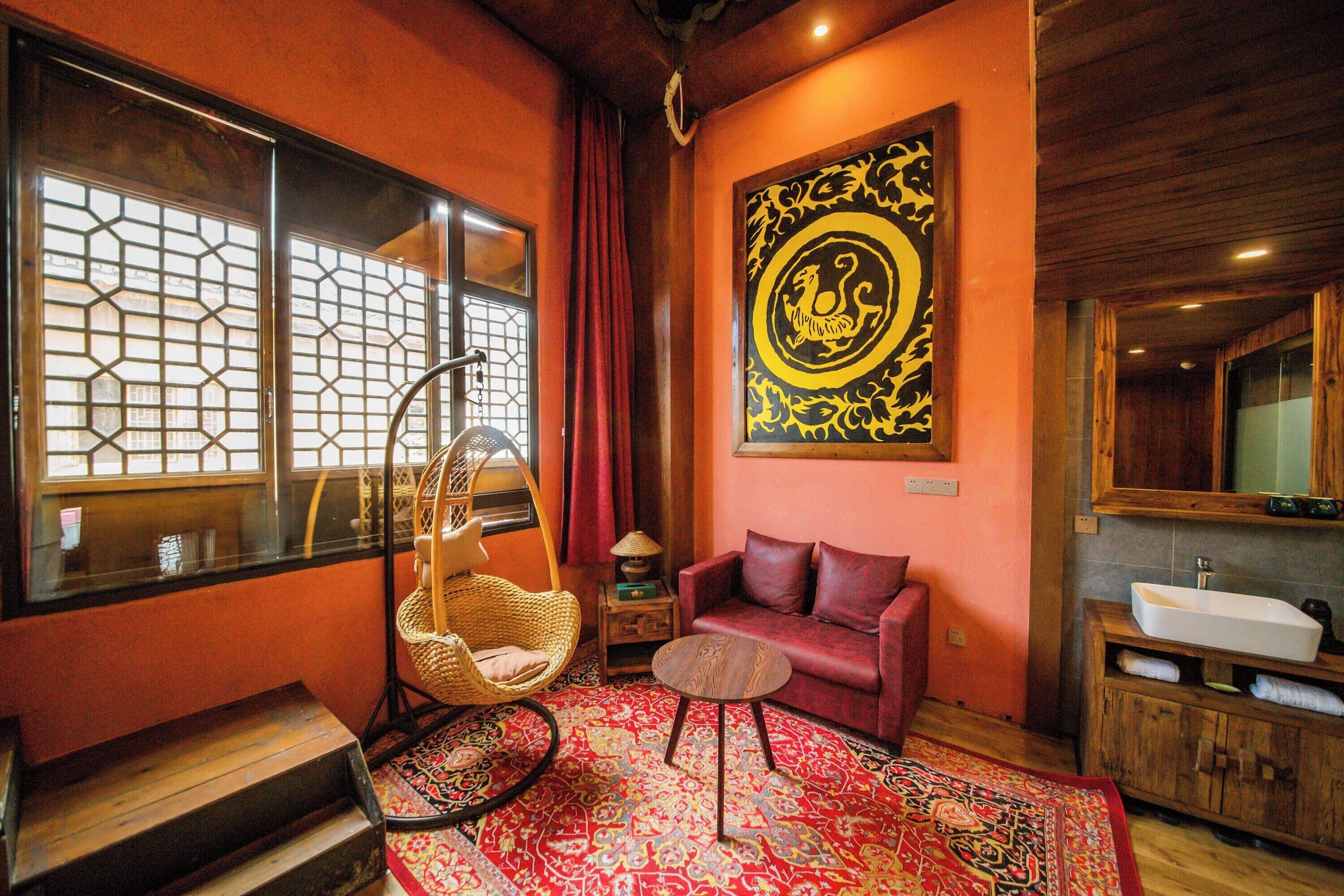 Une pièce au décor traditionnel, comprenant un fauteuil en osier, un canapé rouge, un tapis à motifs, une œuvre d’art accrochée au mur et un meuble en bois avec un évier.