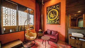 Une pièce au décor traditionnel, comprenant un fauteuil en osier, un canapé rouge, un tapis à motifs, une œuvre d’art accrochée au mur et un meuble en bois avec un évier.
