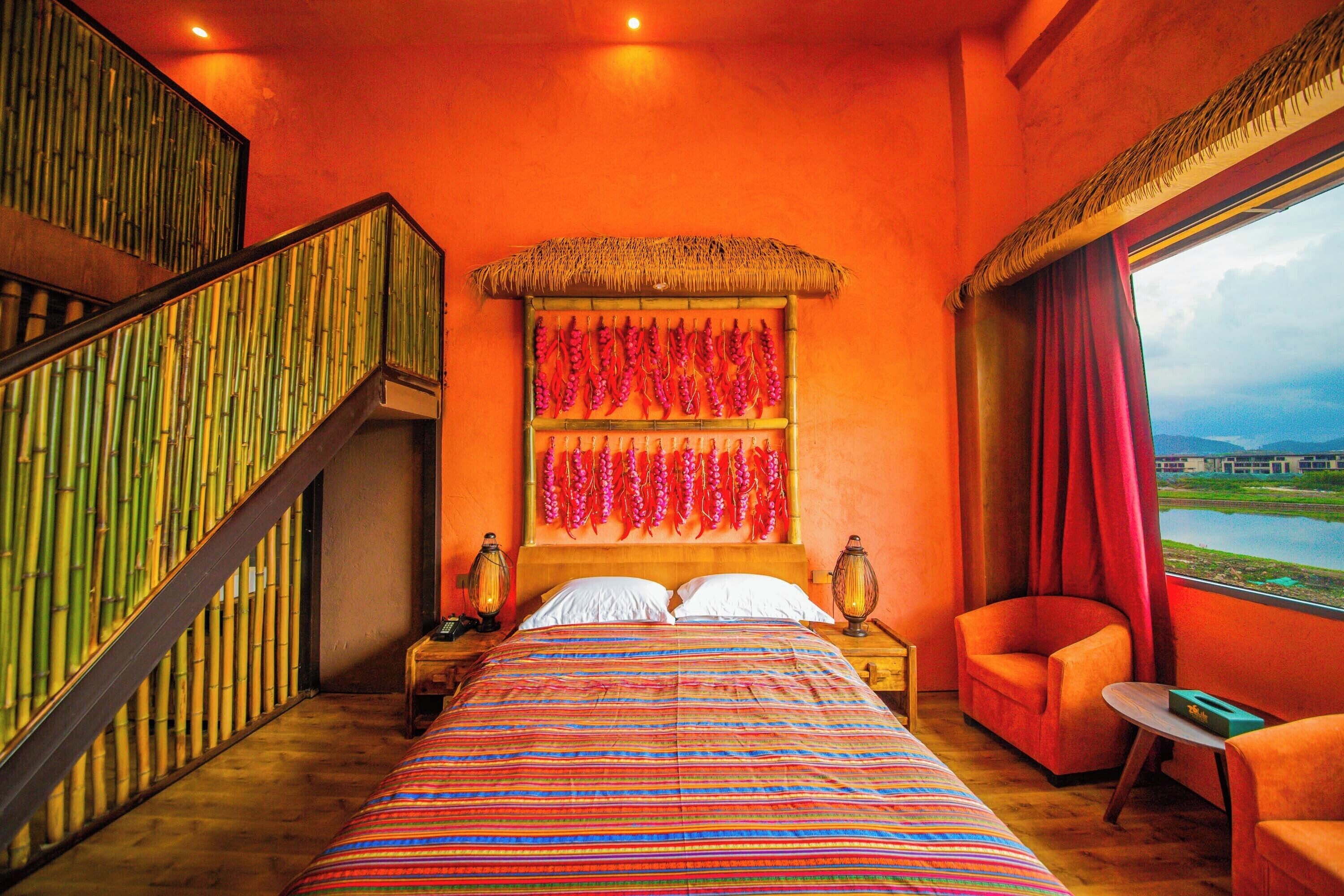 A room with a bed, a chair, a table, a nightstand, a lamp, a window, and a staircase.