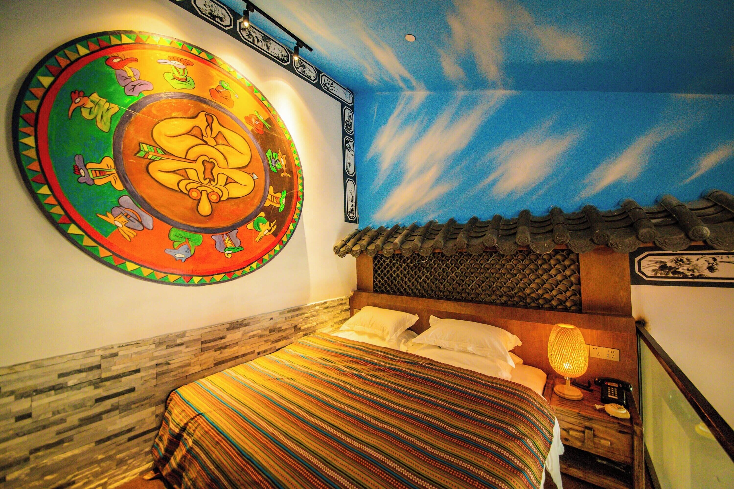 A hotel room with a bed, a wall mural, a nightstand, and a lamp.